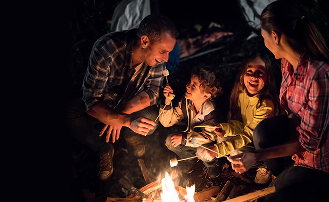 Familie mit Vater, Mutter und zwei Kindern an einem Lagerfeuer, abends, beim Rösten von Marshmallows